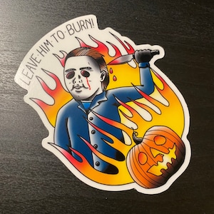 May include: A sticker featuring a cartoon illustration of a masked figure holding a knife, with flames and a pumpkin behind him. The text "LEAVE HIM TO BURN!" is written in a curved arc above the figure.