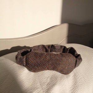 Könnte beinhalten: Ein braunes und blau gemustertes Stirnband liegt auf einer weißen, strukturierten Oberfläche. Das Stirnband besteht aus einem strukturierten Stoff und wirkt weich und bequem. Der Hintergrund ist neutral.