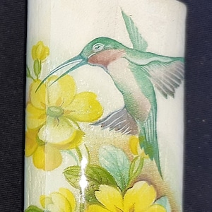 May include: A white lighter with a green hummingbird and yellow flowers printed on the side. The lighter has a silver top and a red button.