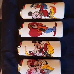 Pode incluir: Quatro isqueiros brancos com diferentes desenhos de personagens da Disney. Os isqueiros apresentam Mickey Mouse, Minnie Mouse, Donald Duck e Pateta.