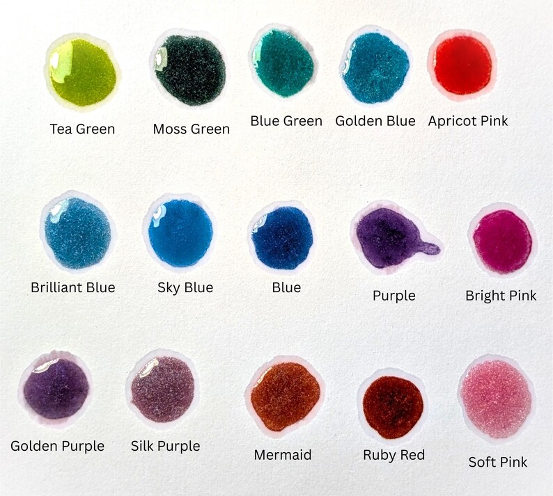 May include: A collection of colorful paint swatches on a white background. The swatches include shades of green, blue, purple, and pink, with names like "Tea Green," "Moss Green," and "Ruby Red" written below each. The paint appears glossy and textured.