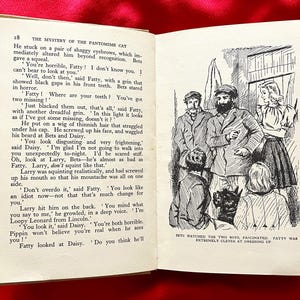 Può includere: Libro aperto con testo e illustrazioni. La pagina sinistra presenta il testo da "The Mystery of the Pantomime Cat". La pagina destra mostra un'illustrazione in bianco e nero di tre uomini e due donne. Il libro è aperto su una superficie rossa.