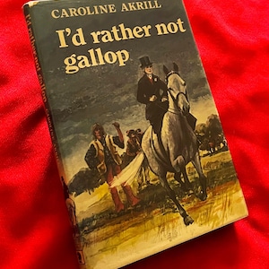 May include: Vintage book titled "I'd Rather Not Gallop" by Caroline Akrill. The cover features an illustration of a person riding a horse, with other figures in the background. The book is set against a red background.
