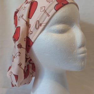 May include: A pink surgical scrub hat with a repeating pattern of red hearts and gold keys.