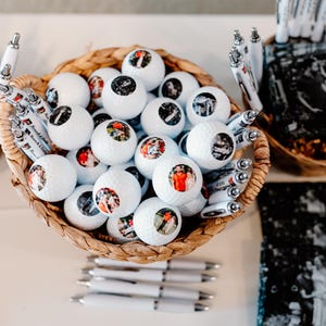 May include: A wicker basket filled with white golf balls, each with a personalized photo. The basket is surrounded by white pens with black ink.