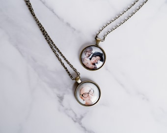 May include: Two gold chain necklaces with round glass pendants featuring photos of people. The pendants are about 1 inch in diameter.