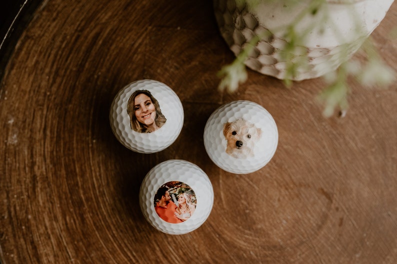 May include: Three white golf balls with personalized photos printed on them. The photos include a woman, a dog, and a couple.