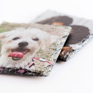 May include: Two slate coasters with a white dog and a black dog printed on them. The coasters have a rough, natural edge.