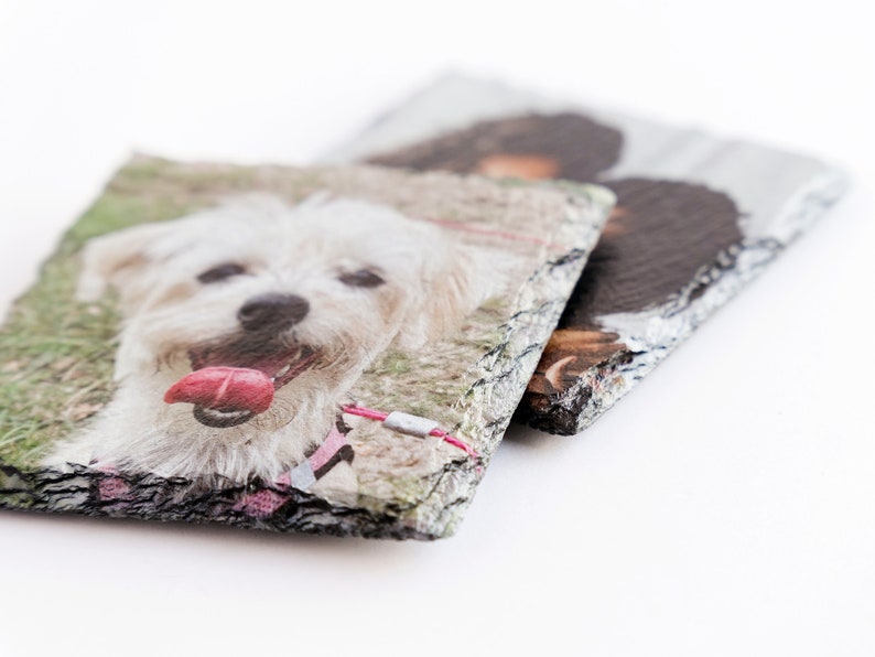 May include: Two slate coasters with a white dog and a black dog printed on them. The coasters have a rough, natural edge.