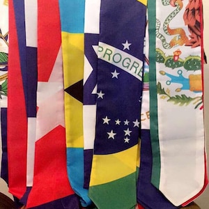 May include: A set of seven graduation sashes in various colours, including blue, red, white, green, and yellow. Each sash features a different country's flag, including the flags of the United States, Cuba, the Bahamas, Brazil, and Mexico.