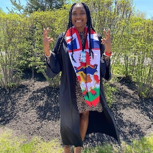 May include: A person wearing a black graduation gown and a colourful sash with a crest. The sash features the flag of Bermuda.