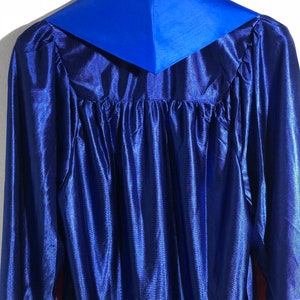 May include: A blue graduation gown with a royal blue collar. The gown is made of a satin-like material.