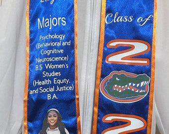 Op de afbeelding: Een blauwe en oranje graduatiessjerp met de tekst "UF Class of 2024" en een alligatorlogo van de University of Florida. De sjerp bevat ook de naam van de afgestudeerde, de majors en een foto van de afgestudeerde in toga en baret.