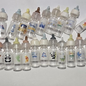 May include: A collection of 20 miniature baby bottles with various designs and labels. The bottles are clear plastic with colorful labels featuring animals, footprints, and brand names like Similac and Avent.