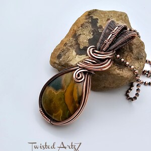 May include: A teardrop-shaped pendant with a copper wire wrap and a brown, green, and yellow agate stone. The pendant is hanging from a copper chain.