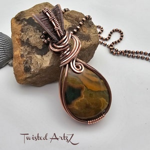 May include: A copper wire wrapped pendant featuring a brown and yellow agate stone. The pendant is attached to a copper chain.