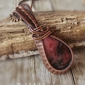May include: A copper wire wrapped pendant featuring a pink and black gemstone. The pendant is hanging from a copper chain.