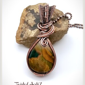 May include: A copper wire wrapped pendant featuring a teardrop-shaped green, brown, and yellow agate stone. The pendant is attached to a copper chain.