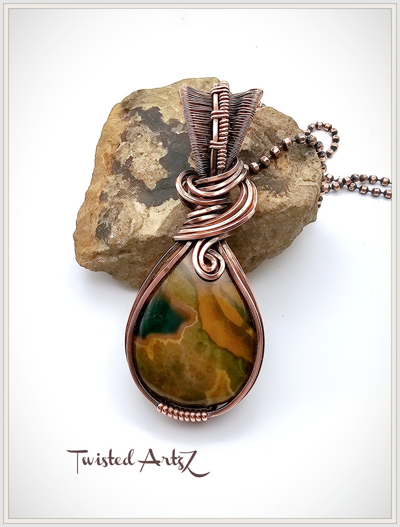 May include: A copper wire wrapped pendant featuring a teardrop-shaped green, brown, and yellow agate stone. The pendant is attached to a copper chain.