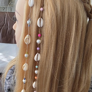May include: Blonde hair with a braid and several strands of decorative hair accessories. The accessories include white seashells, pearls, and colorful beads in pink, purple, blue, and orange.