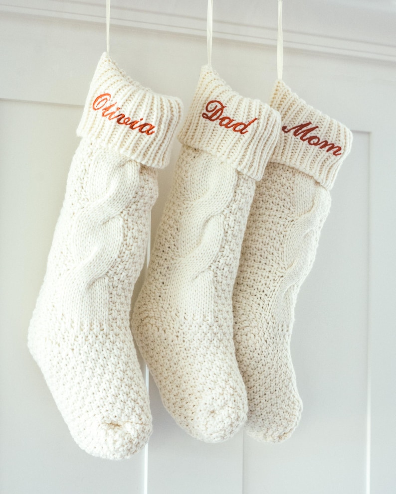 May include: Three white knitted Christmas stockings with the names "Olivia", "Dad", and "Mom" embroidered in red on the cuff.