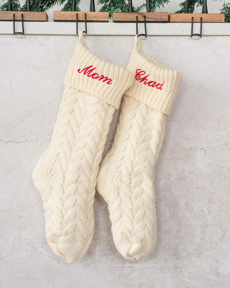 May include: Two white knitted Christmas stockings with red embroidered names, "Mom" and "Chad", hanging on a white wall.