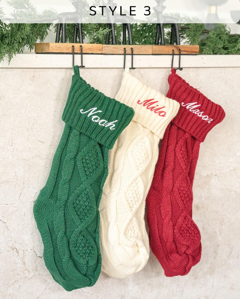 May include: Three knitted Christmas stockings with personalized names, "Noah", "Milo", and "Mason", hanging on a wooden rack. The stockings are green, white, and red.