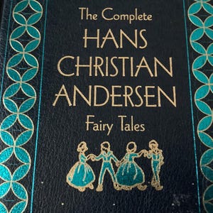 May include: A hardcover book titled "The Complete Hans Christian Andersen Fairy Tales." The cover is dark blue with gold lettering and teal and gold decorative accents. A gold illustration of figures dancing is at the bottom.