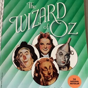 May include: A green book cover with the title "The Wizard of Oz" in white lettering. The cover features four circular images of the characters from the book: Dorothy, the Scarecrow, the Tin Man, and the Cowardly Lion. The book is labeled "The National Bestseller".