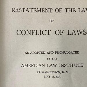 May include: A close-up of a book page with the title "RESTATEMENT OF THE LAW OF CONFLICT OF LAWS." The text is in black font on a cream-colored background. The book was adopted and promulgated by the American Law Institute in Washington, D.C., on May 11, 1934.