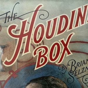 May include: A vintage-style illustration of a red and white sign that reads "The Houdini Box" with the text "by Brian Selznick" in black script below. The sign is set against a blue and white background.