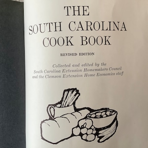 May include: The cover of a vintage cookbook titled "The South Carolina Cook Book, Revised Edition". The cover features a black and white illustration of a loaf of bread, a bowl of fruit, and a pitcher with a bundle of sticks.