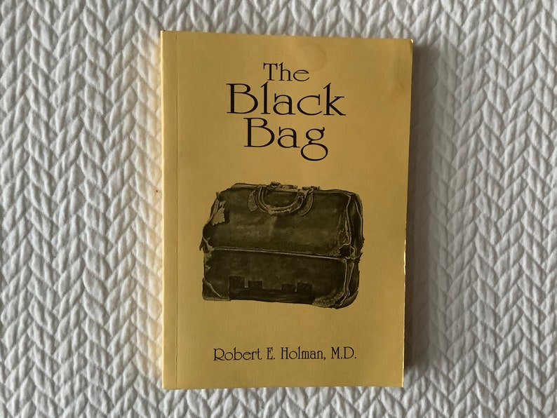 Op de afbeelding: De omslag van een geel boek getiteld "The Black Bag" door Robert E. Holman, M.D. De omslag toont een zwarte leren tas met een versleten en verweerde uitstraling.