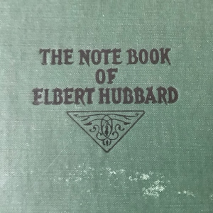 May include: The cover of a green book with the title "The Note Book of Elbert Hubbard" in black lettering.