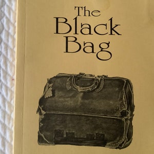 Op de afbeelding: De omslag van een boek getiteld "The Black Bag". De omslag is geel met zwarte tekst en een zwart-witte illustratie van een versleten leren tas.