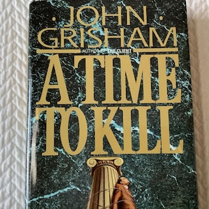 May include: Hardcover book titled "A Time to Kill" by John Grisham. The cover features gold lettering against a dark green marble-like background. A person is tied to a column on the cover.
