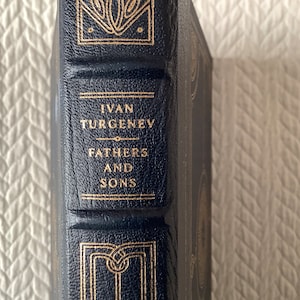 May include: A black leather-bound book with gold lettering on the spine. The title is "Fathers and Sons" by Ivan Turgenev.