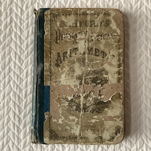 May include: An antique book titled "D. Sanford's Practical Arithmetic" with a distressed cover. The cover is beige and peeling, with blue binding and faded text. The book is a vintage educational item.