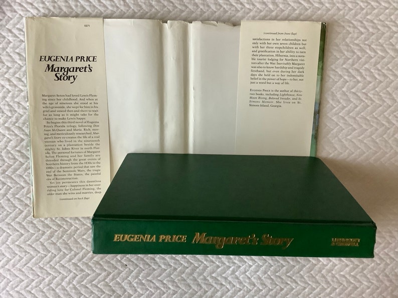 May include: A green hardcover book titled "Eugenia Price Margaret's Story" with gold lettering. The book is closed and the spine is visible. The book is on a white surface.