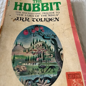 May include: A vintage paperback copy of "The Hobbit" by J.R.R. Tolkien. The cover features a colorful illustration of a landscape with a village, a tree, and a river.