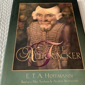 May include: The Nutcracker by E.T.A. Hoffmann, based on a new translation by Aliana Brofmann. The cover features a detailed illustration of the Nutcracker, a wooden toy soldier with a large, toothy grin, wearing a red and gold uniform.