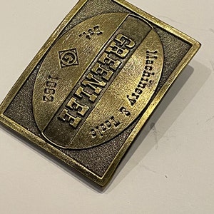 May include: A gold-toned metal belt buckle with the text "EST. 1957" and "SYRACUSE, NY" in a circular design.