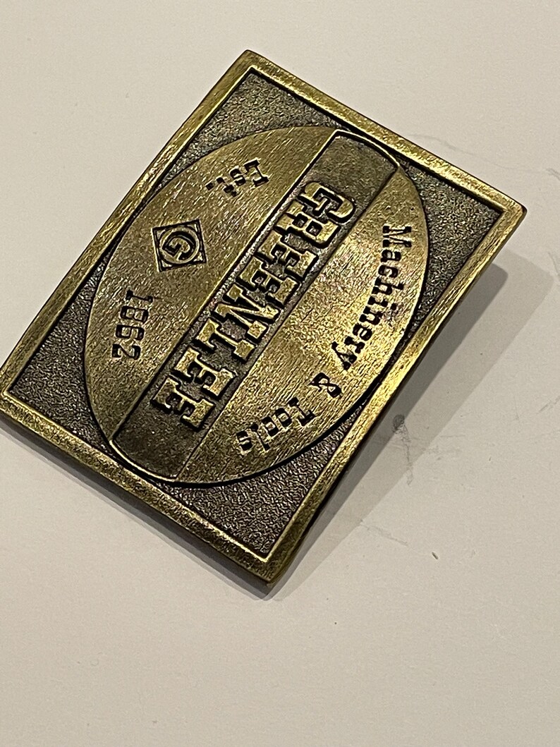 May include: A gold-toned metal belt buckle with the text "EST. 1957" and "SYRACUSE, NY" in a circular design.