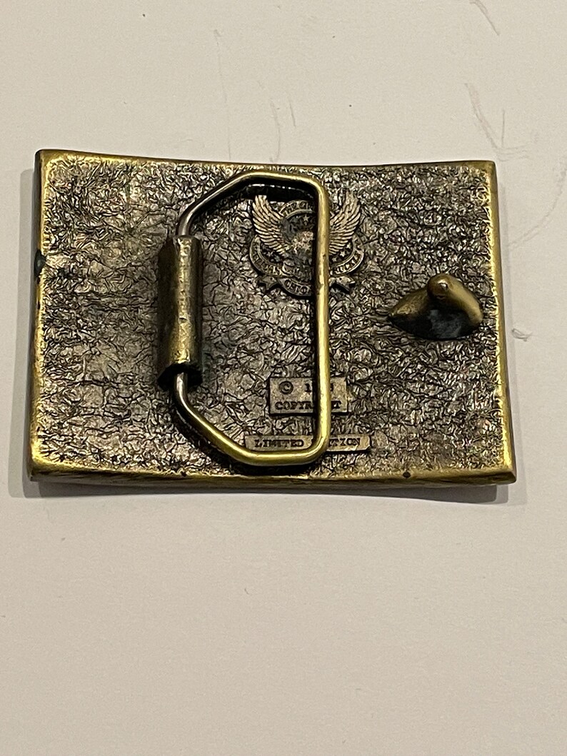 May include: A brass belt buckle featuring an eagle design and the text "Copyright 1981 Limited Edition".