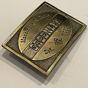 May include: A gold-toned metal belt buckle with the text "G.E.F.E.N.L.A.T.E. Est. 1955" and "Machine W. Tools" engraved on it.