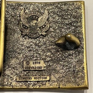 May include: A gold-toned belt buckle with a textured surface. The buckle features an eagle with the text "The Great American Solid Buckle Chicago" and the text "1978 Copyright Limited Edition".