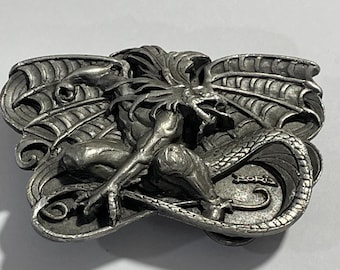 Puede incluir: Una hebilla de cinturón de metal plateado de forma rectangular con una escultura en relieve de una criatura alada con una cola larga. La criatura tiene rasgos afilados y está centrada. El nombre Boris está grabado en la esquina inferior derecha.