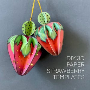 May include: Two three-dimensional paper strawberry ornaments with red bodies, green leaves, and yellow seeds, suspended by gold strings. The text DIY 3D PAPER STRAWBERRY TEMPLATES is printed in white on the right side of the image.