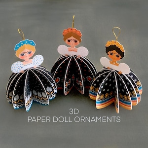 May include: Three 3D paper doll ornaments featuring figures with floral headpieces and white puffed sleeves. Each doll wears a black skirt with colorful floral patterns and a gold hanging loop. The text 3D PAPER DOLL ORNAMENTS is visible.