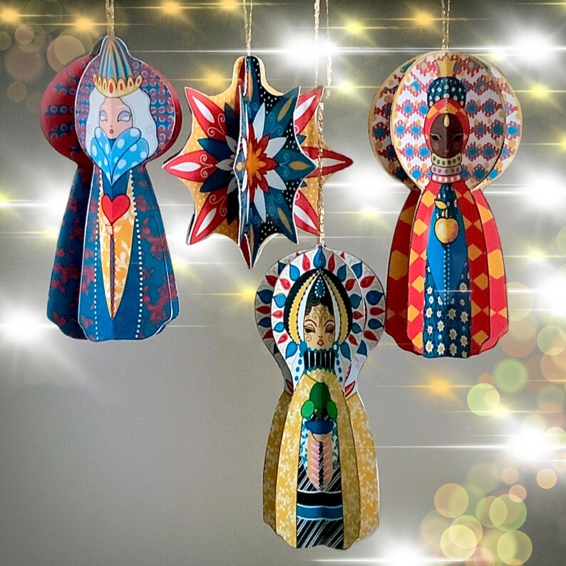 May include: Four hanging ornaments featuring three stylized figures and one multi-pointed star. The figures wear intricate, colorful patterned robes and headpieces. The star displays a geometric design in red, blue, and white. Each piece hangs by a gold cord.